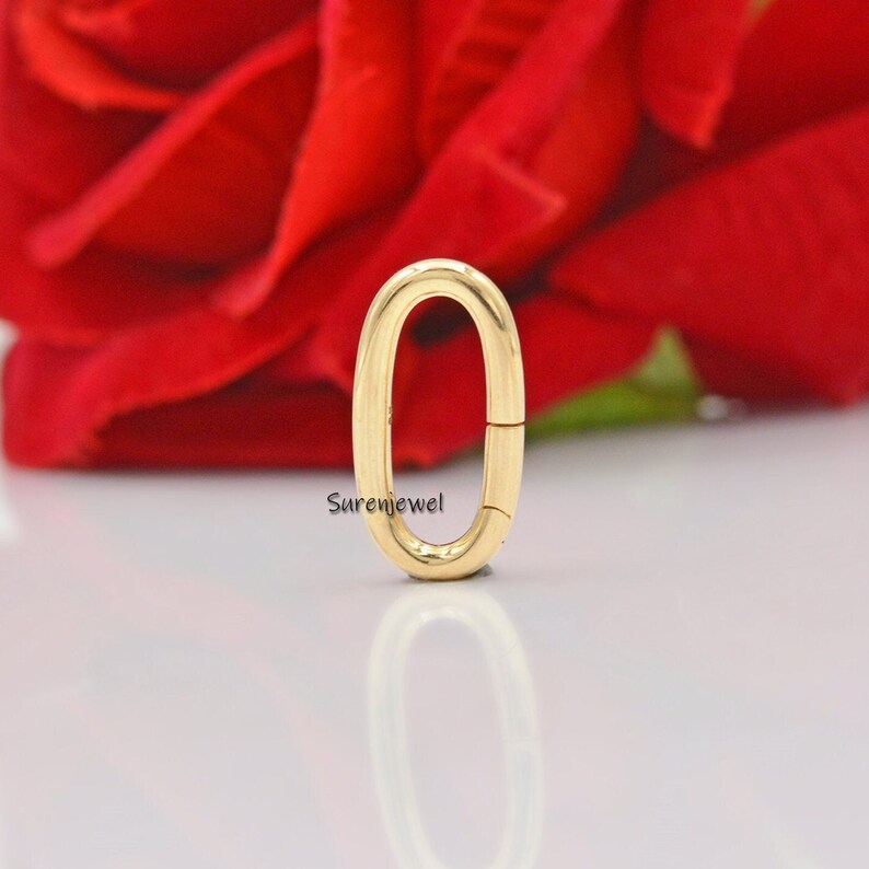 May include: Gold oval shaped clasp for a necklace or bracelet. The clasp is open and ready to be attached to a chain.