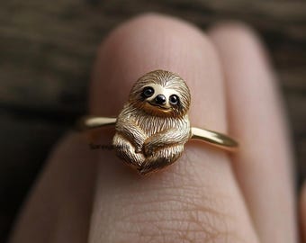 Può includere: Anello in oro con una scultura dettagliata di un bradipo. Il bradipo è seduto con le braccia incrociate e ha un'espressione amichevole.