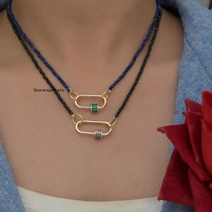May include: Two layered necklaces with black and blue beads. The necklaces feature a gold oval pendant with a green and pink stone.