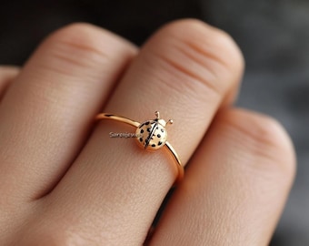 May include: A gold ring with a small ladybug design. The ladybug is black with white spots.