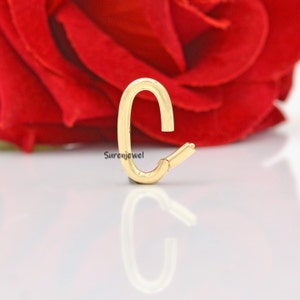 May include: Gold-toned metal letter C charm. The charm is shaped like the letter C and has a smooth, polished finish.