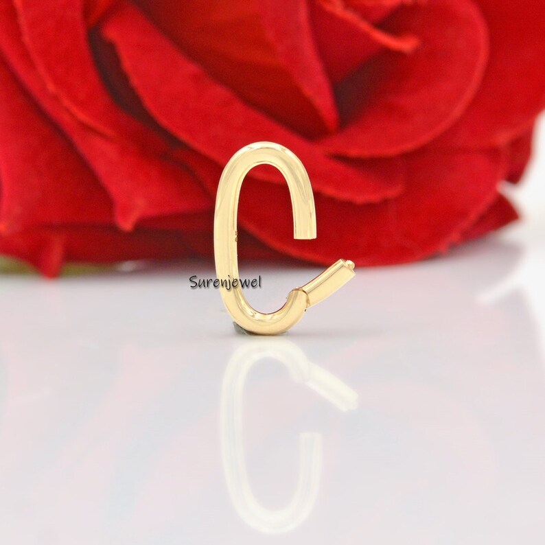 May include: Gold-toned metal letter C charm. The charm is shaped like the letter C and has a smooth, polished finish.