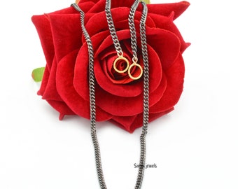 May include: A black chain necklace with two gold rings hanging from it. The necklace is lying on a red rose.