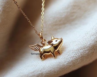 May include: A gold necklace with a pendant of a pig with wings. The pig is facing to the right and has a small snout.