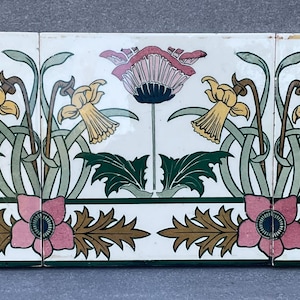 Puede incluir: Un conjunto de tres baldosas cerámicas rectangulares con un diseño floral. El diseño incluye flores rosas y moradas, narcisos amarillos, hojas verdes y un borde con flores rosas y hojas marrones. Las baldosas están dispuestas una al lado de la otra.