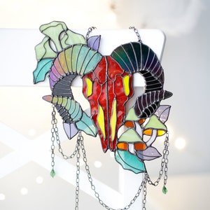 May include: A stained glass ram skull with iridescent green, blue, and purple leaves and mushrooms hanging from a silver chain with green glass beads.