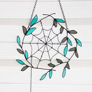 May include: A stained glass spider web with teal leaves hanging from a chain with a small stained glass spider at the bottom.