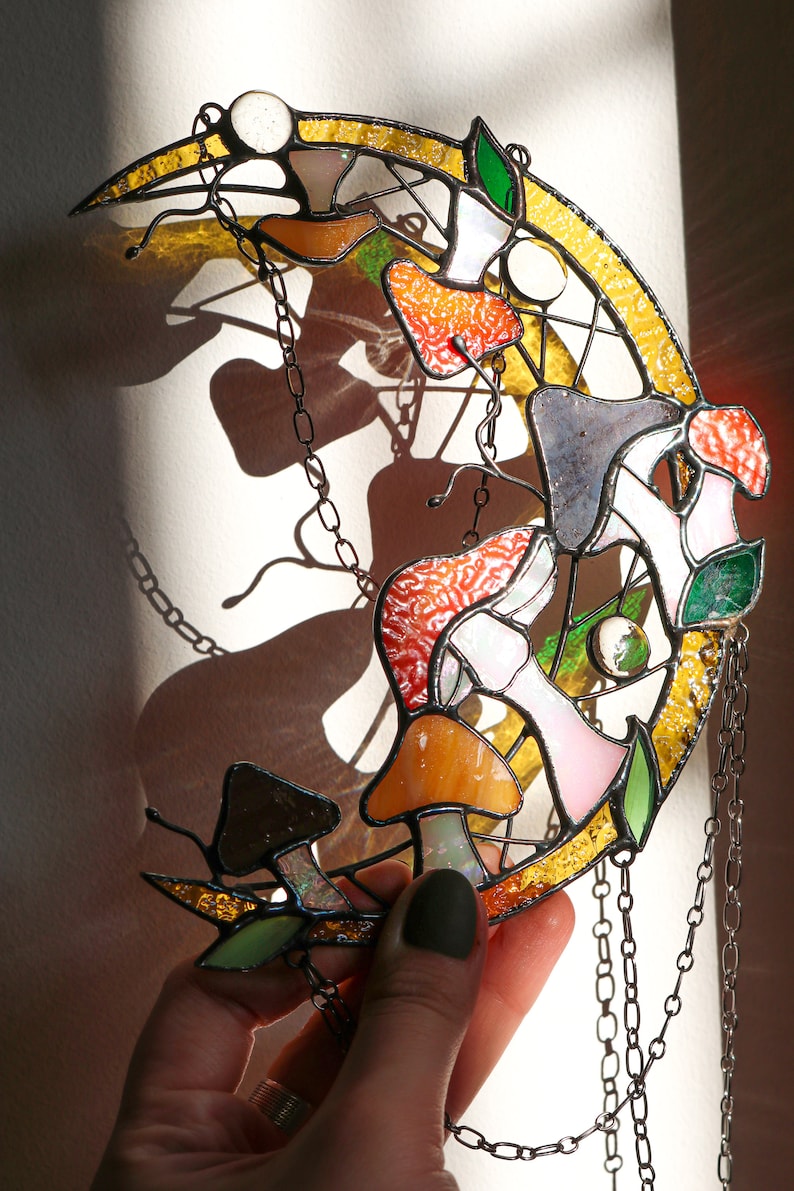 Puede incluir: Una luna de vidrio coloreado con una cadena colgando de ella. La luna est&aacute; decorada con setas de varios colores, incluyendo rojo, naranja, amarillo, rosa y verde.
