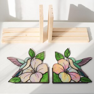 Pu&ograve; includere: Un paio di fermalibri in vetro colorato con colibr&igrave; e fiori con una libreria in legno. I fermalibri presentano un colibr&igrave; con ali verdi, viola e blu e un grande fiore rosa e giallo. La libreria in legno &egrave; in legno non rifinito.