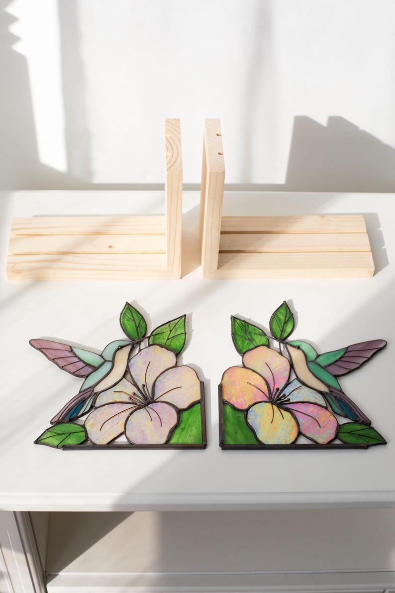Pu&ograve; includere: Un paio di fermalibri in vetro colorato con colibr&igrave; e fiori con una libreria in legno. I fermalibri presentano un colibr&igrave; con ali verdi, viola e blu e un grande fiore rosa e giallo. La libreria in legno &egrave; in legno non rifinito.