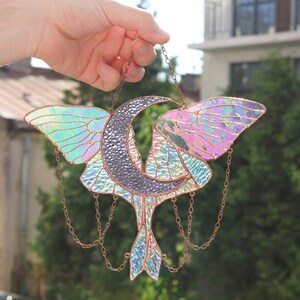May include: A stained glass suncatcher featuring a crescent moon and a butterfly with iridescent wings. The suncatcher is suspended from a copper chain.