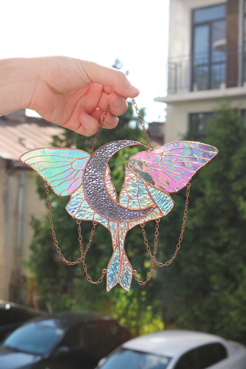 May include: A stained glass suncatcher featuring a crescent moon and a butterfly with iridescent wings. The suncatcher is suspended from a copper chain.