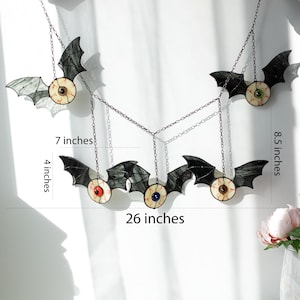 May include: A hanging mobile featuring five stained glass bats with realistic eyeballs, connected by metal chains. The total width is 66 cm, with individual bat heights of 10 cm and 22 cm, and a 18 cm spacing between the hanging elements.