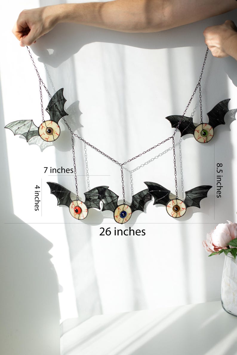 May include: A hanging mobile featuring five stained glass bats with realistic eyeballs, connected by metal chains. The total width is 66 cm, with individual bat heights of 10 cm and 22 cm, and a 18 cm spacing between the hanging elements.