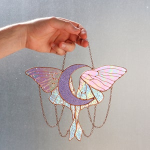 May include: A stained glass moon and moth suncatcher with iridescent wings and a purple crescent moon. The suncatcher is hanging from a copper chain.
