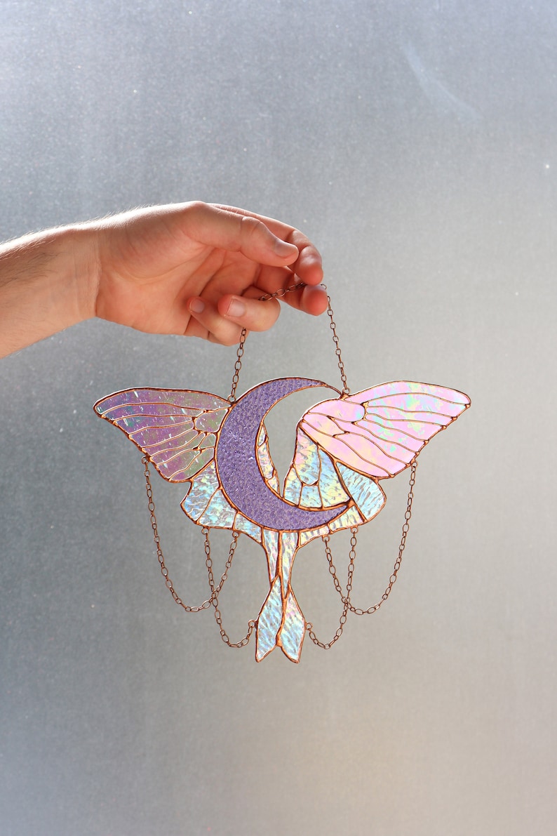 May include: A stained glass moon and moth suncatcher with iridescent wings and a purple crescent moon. The suncatcher is hanging from a copper chain.