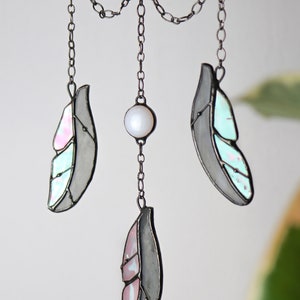 May include: A stained glass dreamcatcher with three feathers and a pearl bead hanging from a chain. The feathers are gray with pink and blue accents.