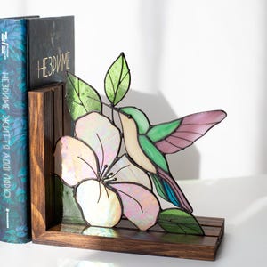 Pu&ograve; includere: Reggilibri con colibr&igrave; e fiore in vetro colorato. Il colibr&igrave; ha ali verdi, rosa e blu, con un corpo color crema. Il fiore &egrave; bianco e rosa. Il reggilibri &egrave; in legno scuro.