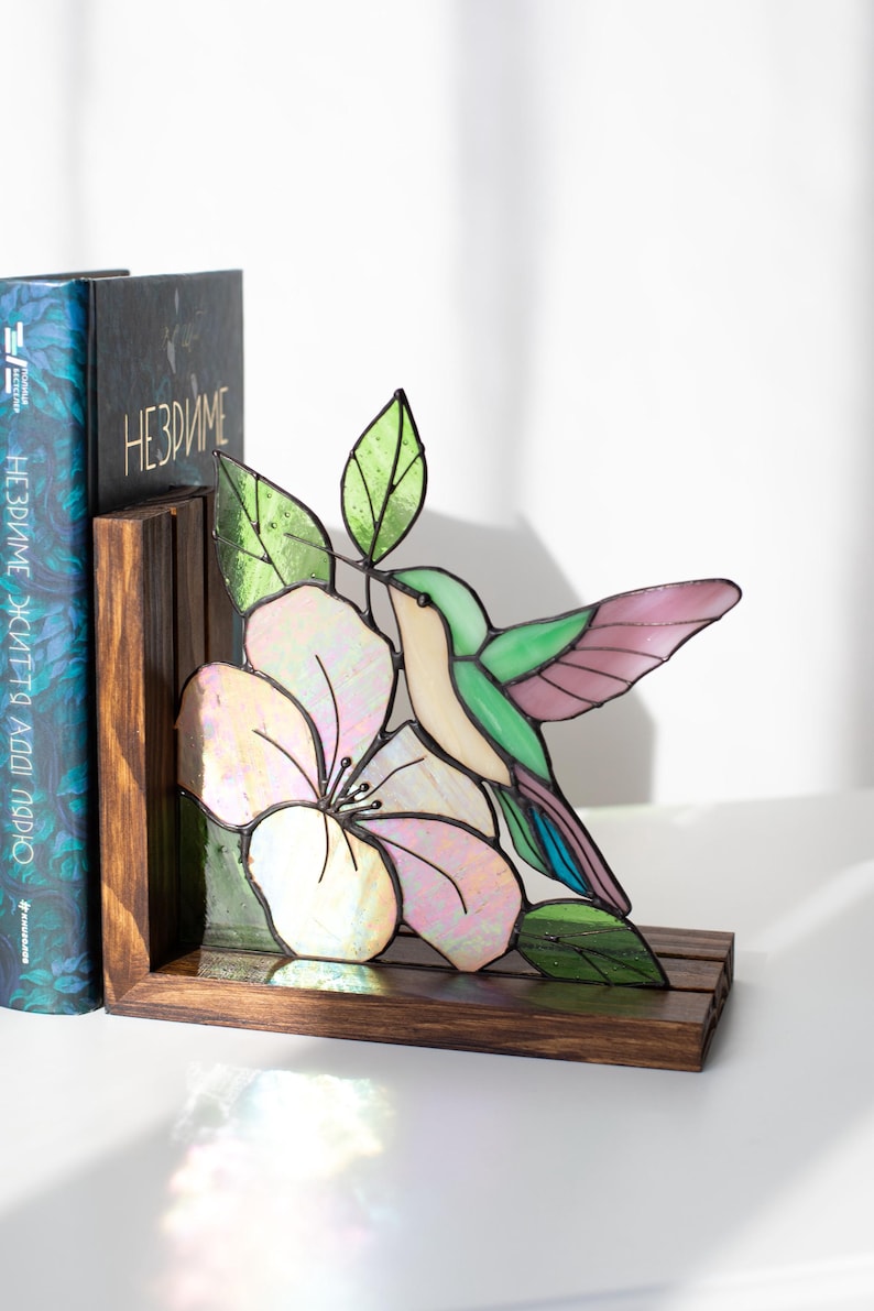 Pu&ograve; includere: Reggilibri con colibr&igrave; e fiore in vetro colorato. Il colibr&igrave; ha ali verdi, rosa e blu, con un corpo color crema. Il fiore &egrave; bianco e rosa. Il reggilibri &egrave; in legno scuro.