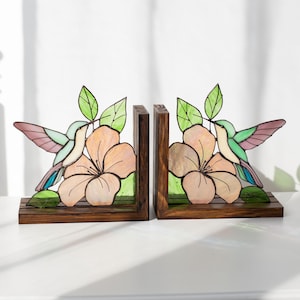 Pu&ograve; includere: Un paio di fermalibri in legno con un design a vetrate. Ogni fermalibri presenta un colibr&igrave;, un grande fiore e foglie verdi. Il colibr&igrave; ha ali rosa, blu e verdi. Il fiore &egrave; color pesca.