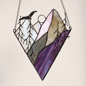 May include: A stained glass window hanging from a chain, depicting a purple, pink, and brown mountain range with a black bird flying overhead.