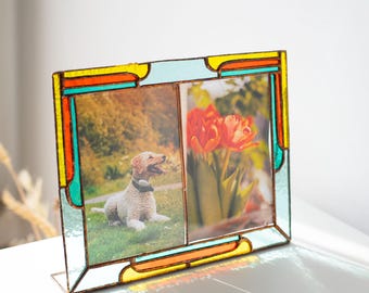 May include: A stained glass double photo frame with a colorful design. The frame features a light blue, yellow, orange, and teal border. One side holds a photo of a dog, and the other side holds a photo of red tulips.