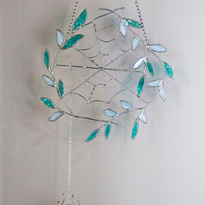 May include: A silver metal spider web with teal and white glass leaves hanging from a silver chain. A silver spider charm hangs from the bottom of the web.