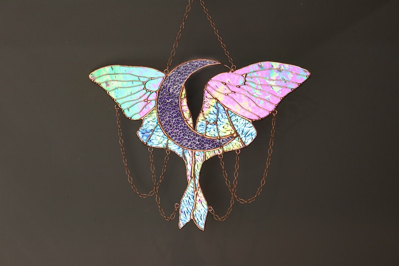 May include: A stained glass moon and butterfly suncatcher with iridescent blue, pink, and purple glass. The suncatcher is suspended from a chain.