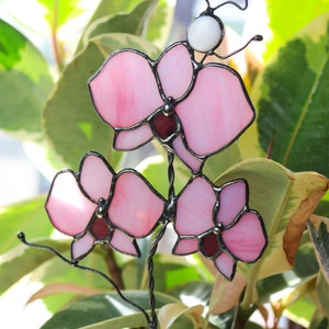 K&ouml;nnte beinhalten: Eine rosafarbene Orchideenbl&uuml;te aus Glasmalerei mit einer wei&szlig;en Perle an der Spitze des Stiels. Die Orchidee besteht aus Glas und Draht und ist ein Dekorationsst&uuml;ck.