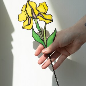 May include: A stained glass flower with yellow petals and green leaves, attached to a black metal stem.