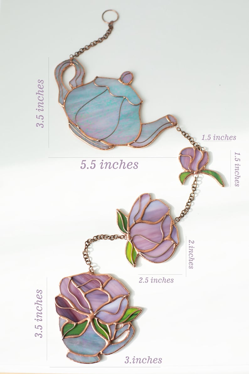 Puede incluir: Un adorno colgante de vitral con una tetera y tres flores conectadas por cadenas de cobre. La tetera mide 8,9 cm por 14 cm. Las flores var&iacute;an de 3,8 cm a 8,9 cm de altura y de 3,8 cm a 7,6 cm de ancho.