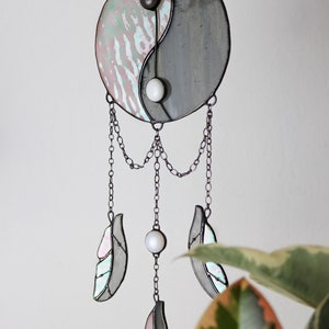 May include: A stained glass yin yang symbol with iridescent glass and black and white beads hangs from a chain with three iridescent glass feathers.
