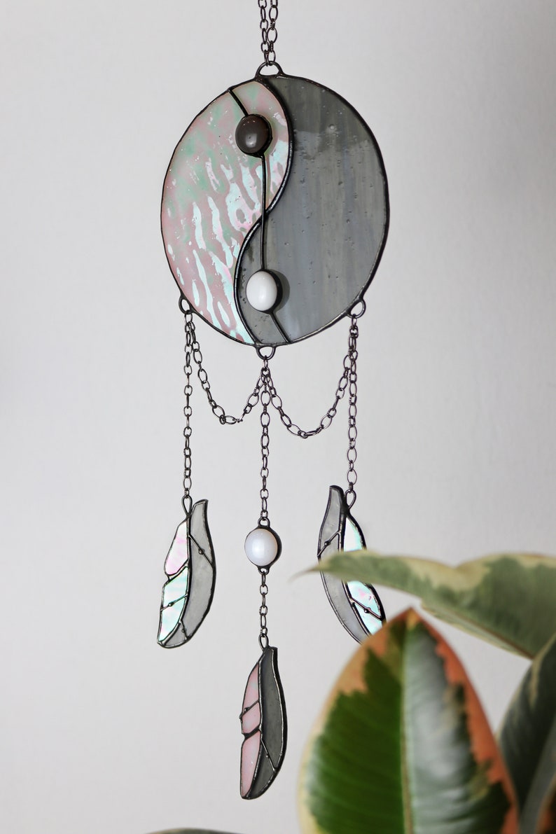 May include: A stained glass yin yang symbol with iridescent glass and black and white beads hangs from a chain with three iridescent glass feathers.