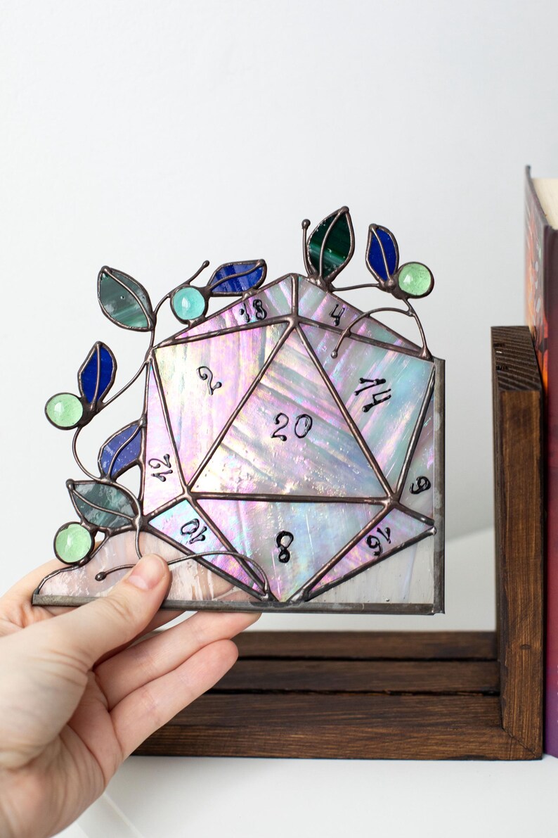 May include: Stained glass D20 die with iridescent glass and a decorative vine with blue, green, and teal accents. The die is a corner piece, with numbers visible on the facets. A unique piece for tabletop gaming enthusiasts.