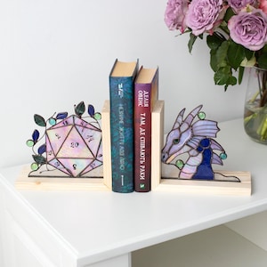 May include: Stained glass D20 dice and dragon bookends on a wooden base. The bookends are holding two books. A vase of purple roses sits on the right side of the table.