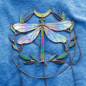 May include: A stained glass dragonfly suncatcher with iridescent wings, a crescent moon, and green leaves. The suncatcher is suspended from a chain.