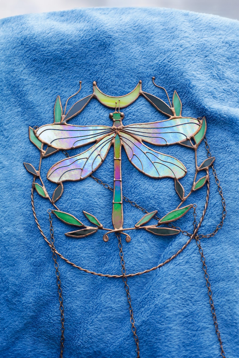 May include: A stained glass dragonfly suncatcher with iridescent wings, a crescent moon, and green leaves. The suncatcher is suspended from a chain.