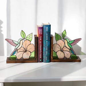 Pu&ograve; includere: Reggilibri con colibr&igrave; e fiori in vetro colorato. I reggilibri sono in legno e presentano un colorato design di colibr&igrave; con accenti rosa, verdi e viola. I reggilibri sostengono tre libri.