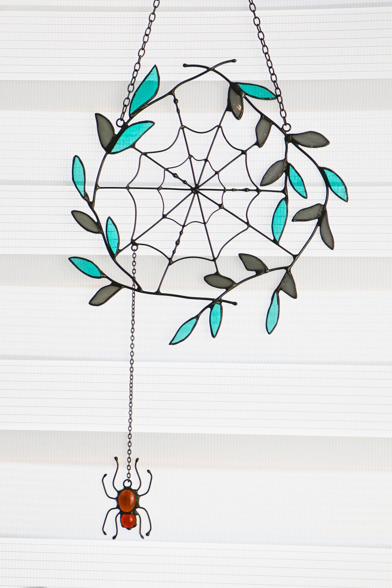 May include: A stained glass spider web with teal leaves hanging from a chain with a small stained glass spider at the bottom.