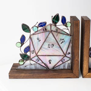 May include: Stained glass D20 bookends with a wooden base. The iridescent glass die features numbers and is accented with green and blue leaves and orbs. A unique decorative item for tabletop gamers.