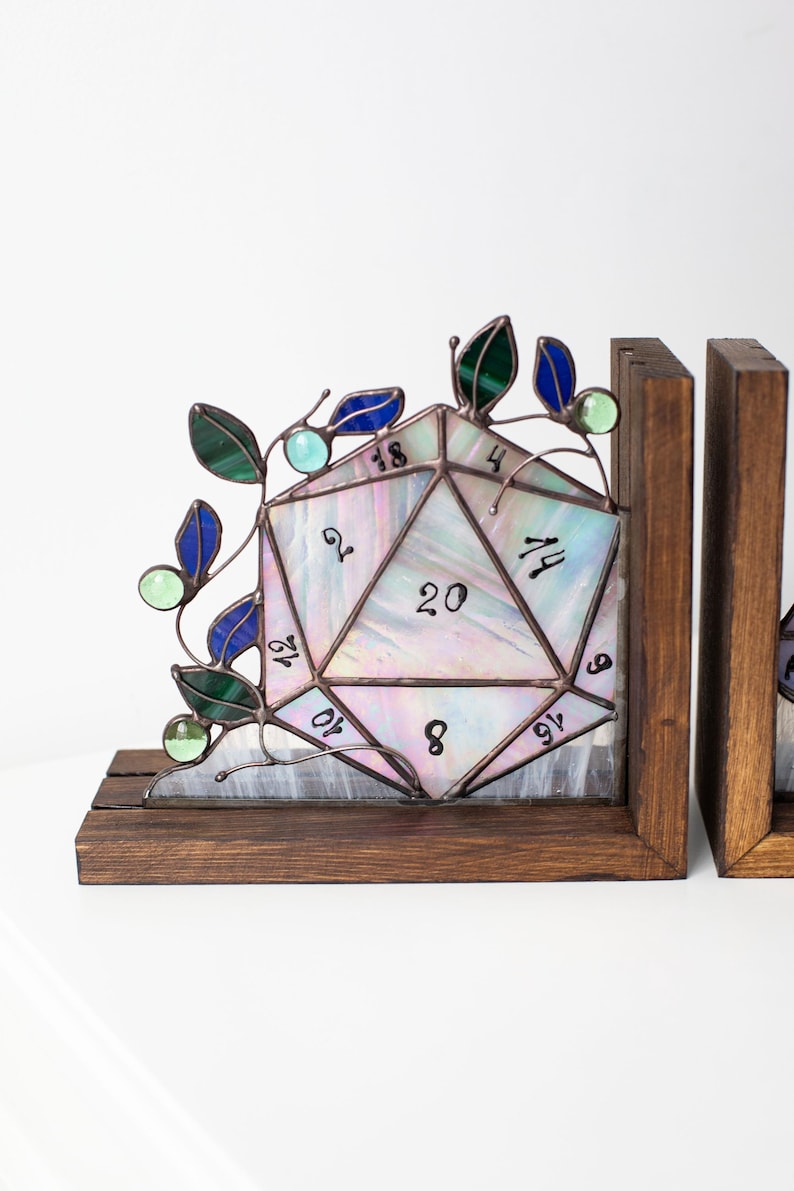May include: Stained glass D20 bookends with a wooden base. The iridescent glass die features numbers and is accented with green and blue leaves and orbs. A unique decorative item for tabletop gamers.