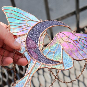 May include: A stained glass suncatcher featuring a crescent moon and iridescent butterfly wings. The suncatcher is suspended from a copper chain.