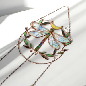 May include: A stained glass dragonfly suncatcher with iridescent wings, a crescent moon, and green leaves. The suncatcher hangs from a copper chain with a purple crystal bead.