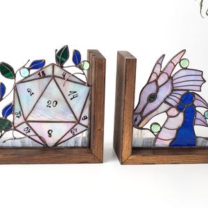 May include: Stained glass bookends featuring a D20 die and a dragon head. The die is white with black numbers and green and blue accents. The dragon is purple, blue, and green. Both are set in wooden frames.