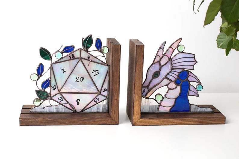 May include: Stained glass bookends featuring a D20 die and a dragon head. The die is white with black numbers and green and blue accents. The dragon is purple, blue, and green. Both are set in wooden frames.