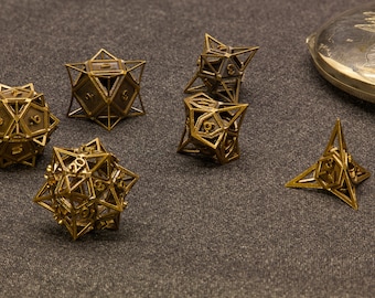 Pode incluir: Seis dados de metal dourado com diferentes números de faces. Os dados estão sobre uma superfície cinza.