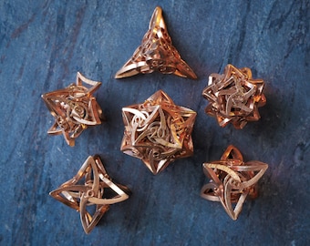 May include: A set of six metallic copper-colored polyhedral dice featuring intricate, open-work geometric frames. Each die displays engraved numbers, including a prominent 20 on the central piece, with complex, interlocking structural designs.