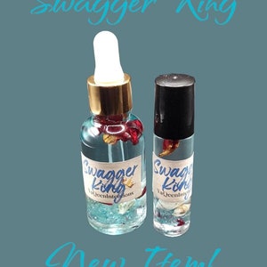 May include: Two bottles of essential oil, one in a glass dropper bottle and one in a roller bottle. Both bottles are clear and contain a blue liquid with glitter and red flower petals. The labels on the bottles read "Swagger King YaQueenIntentions".
