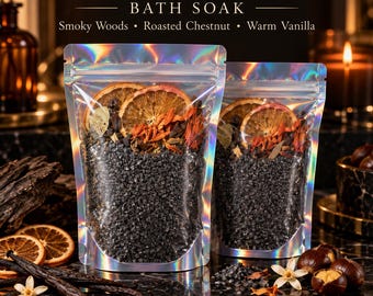 Pode incluir: Dois sacos holográficos de Banish Inner Demon Bath Soak contendo sal preto, fatias de laranja seca e botânicos. O texto diz Banish Inner Demon Bath Soak, Smoky Woods, Roasted Chestnut e Warm Vanilla. Os sacos são transparentes.