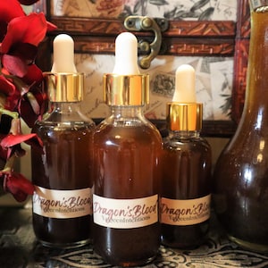 May include: Three glass bottles with gold lids and droppers filled with a dark brown liquid. The bottles are labeled "Dragon's Blood" and "Yggdrasil Intentions".
